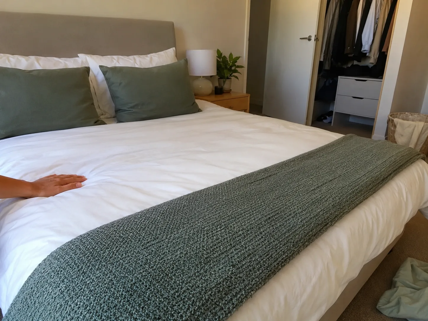Neatly made bed with white bedding, green pillows and a folded green blanket in a tidy bedroom.