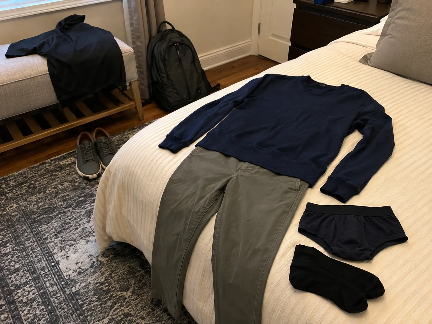 Tomorrow’s outfit laid out on a bed with a jumper, trousers, underwear, socks, shoes and a backpack ready nearby.
